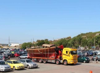 The Benefits of Reliable Vehicle Shipping Services in Idaho for Moms and Families Yellow truck hauling wooden boat in parking lot.