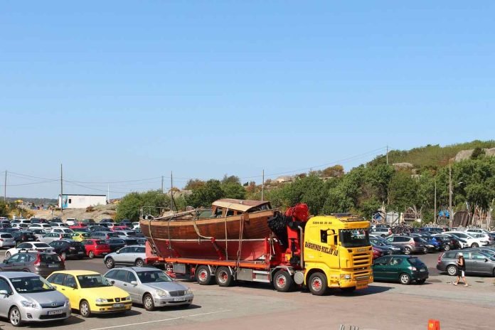 Benefits of Reliable Vehicle Shipping Services Yellow truck hauling wooden boat in parking lot.