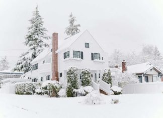 Blizzard Busters: 6 Genius Tips To Protect Your Home From Snow Damage Snow-covered residential house with trees and shrubs after a heavy snowfall.