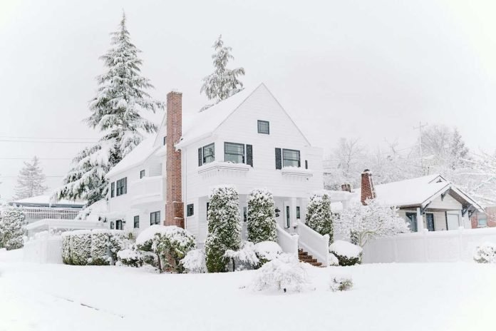 Protect Your Home From Snow Damage Snow-covered residential house with trees and shrubs after a heavy snowfall.
