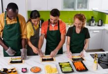 What a New Orleans Hands-on Cooking Class Looks Like Four diverse adults wearing aprons participate in a sushi-making class in a modern kitchen.