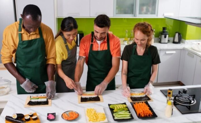 What a New Orleans Hands-on Cooking Class Looks Like Four diverse adults wearing aprons participate in a sushi-making class in a modern kitchen.