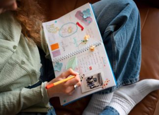 The Ultimate Pregnancy Memory Checklist (That Doesn’t Involve Scrapbooking) Woman journaling with colorful scrapbook elements in a notebook.