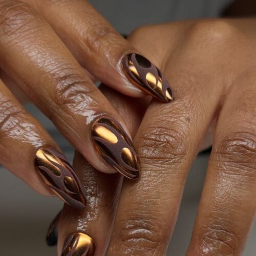 Close-up of hands with brown and metallic gold flame-patterned textured nails.