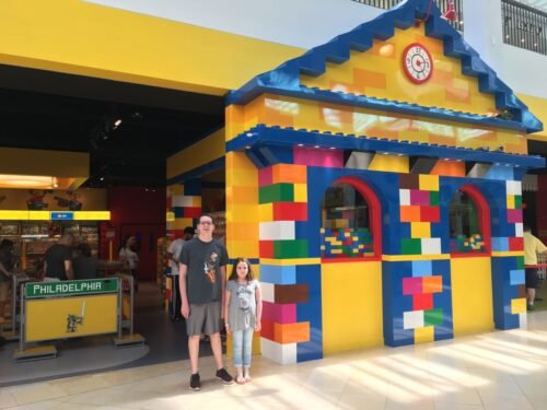 Two children standing in front of a LEGO-themed building inside LEGO Discovery Center.