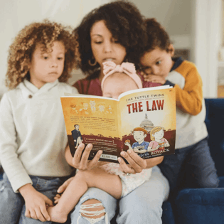 A mother reading "The Tuttle Twins: The Law" book to her children on a sofa.